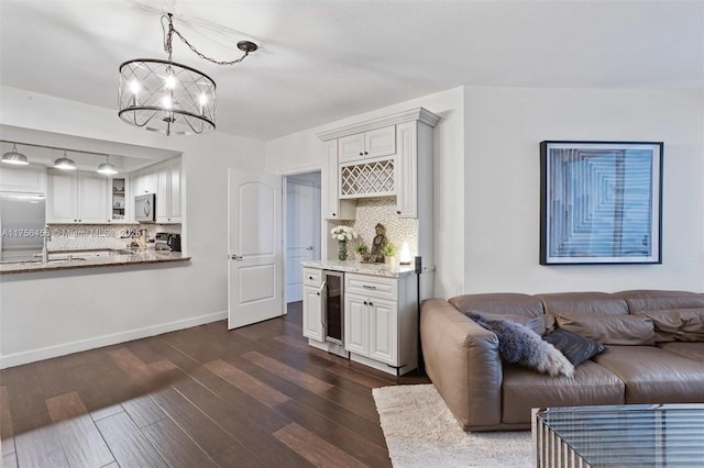 living room featuring a notable chandelier, beverage cooler, dark wood-style flooring, baseboards, and a dry bar