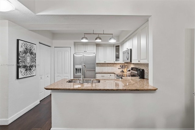 kitchen with light stone counters, dark wood-style flooring, a sink, appliances with stainless steel finishes, and backsplash