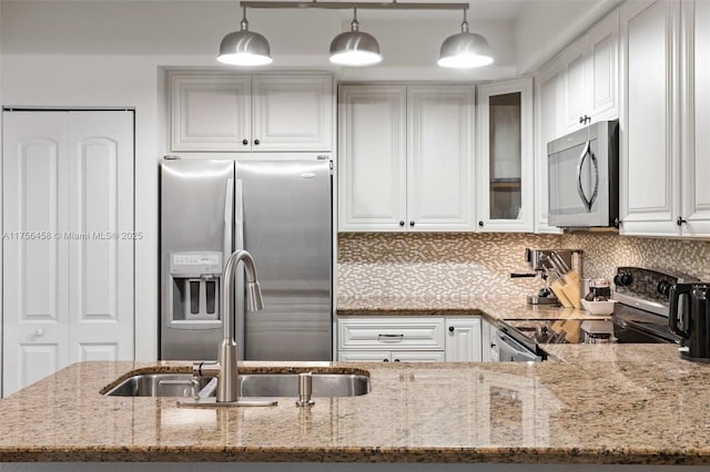 kitchen with stainless steel appliances, glass insert cabinets, a sink, and light stone countertops