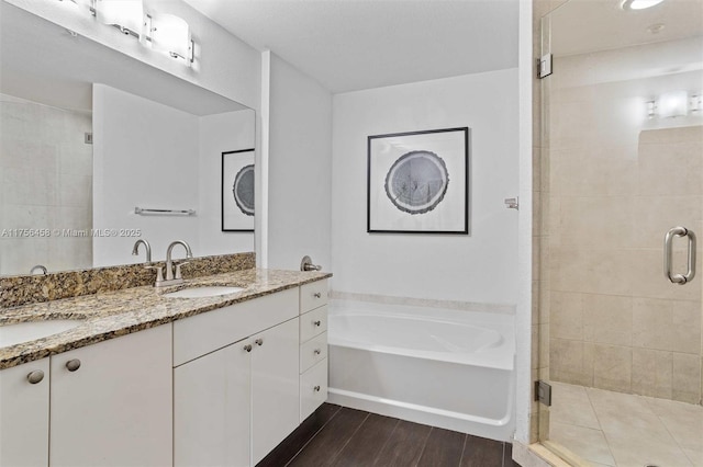 full bathroom with a garden tub, double vanity, a sink, a shower stall, and wood finished floors