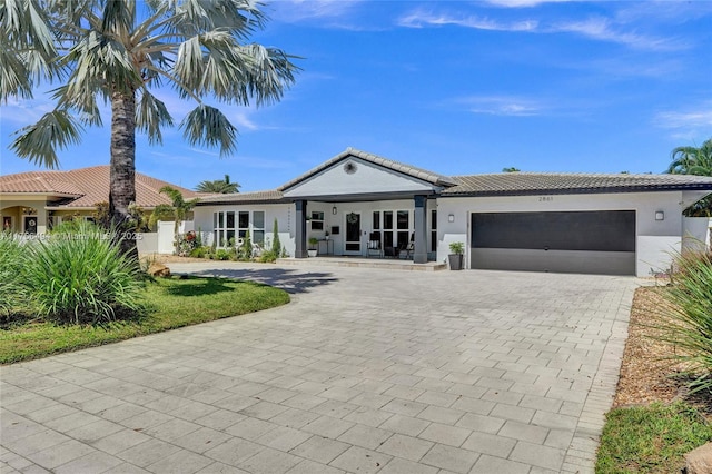 view of front of property featuring a tiled roof, decorative driveway, an attached garage, and stucco siding