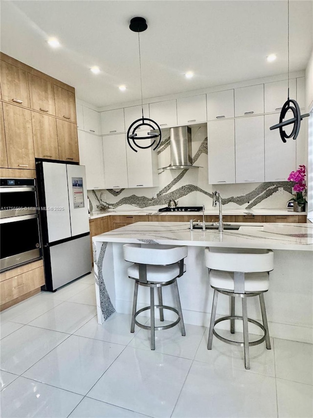 kitchen featuring wall chimney exhaust hood, a kitchen bar, double oven, and freestanding refrigerator