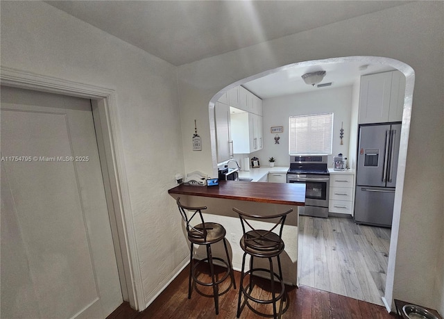 kitchen featuring stainless steel appliances, arched walkways, a sink, and wood finished floors