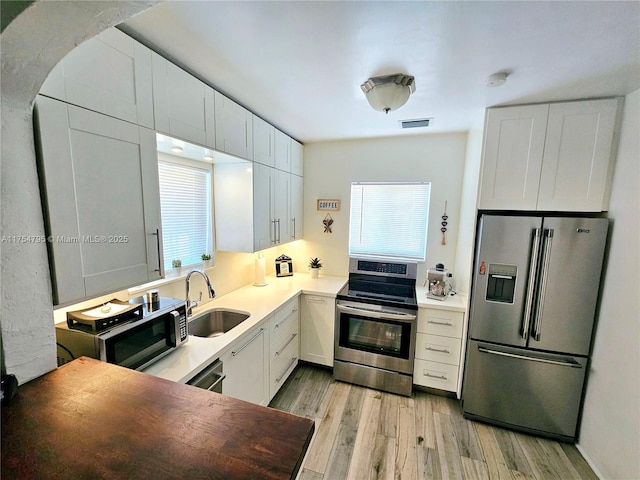 kitchen featuring light wood finished floors, visible vents, white cabinets, appliances with stainless steel finishes, and a sink