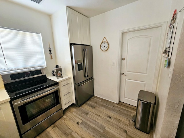 kitchen with stainless steel appliances, light countertops, light wood-style flooring, and white cabinetry