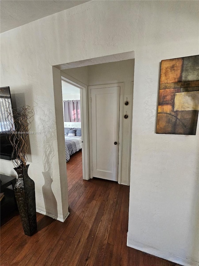 corridor featuring a textured wall and dark wood-style flooring