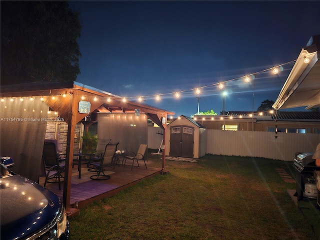 yard at night with a fenced backyard, a storage shed, an outdoor structure, a wooden deck, and outdoor dining space