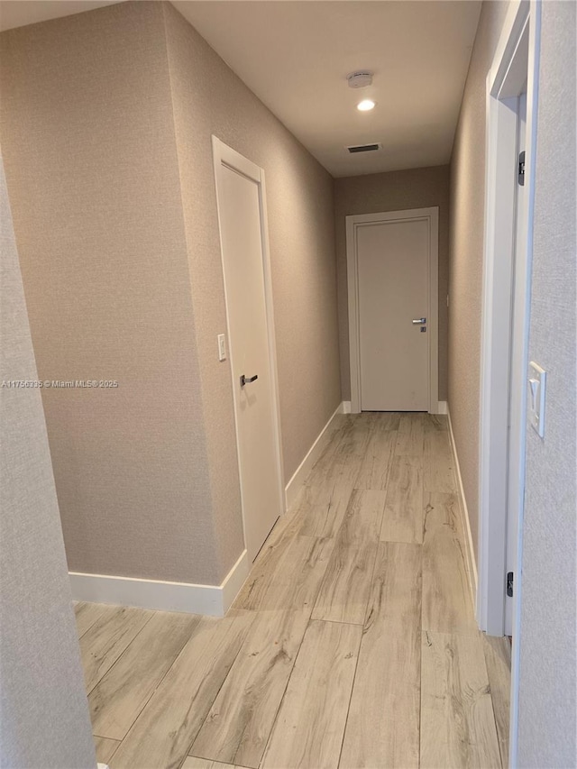 hall with light wood-style flooring, visible vents, and baseboards