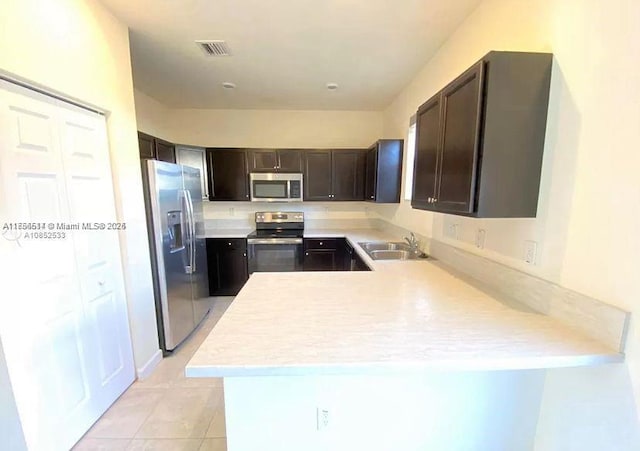 kitchen with appliances with stainless steel finishes, dark brown cabinets, a sink, and light countertops