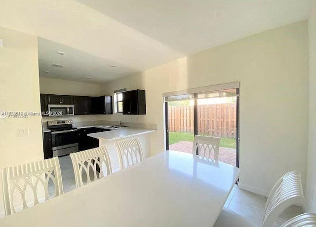 kitchen featuring light tile patterned floors, stainless steel appliances, light countertops, a sink, and dark cabinets