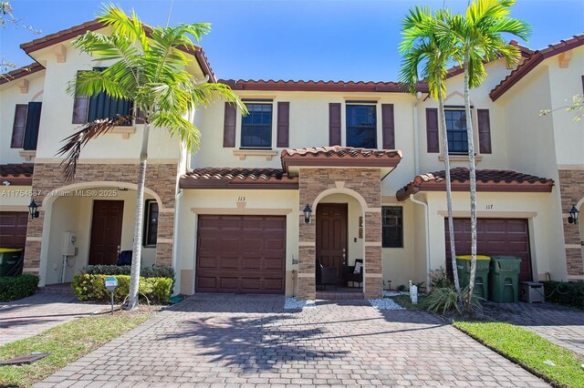 mediterranean / spanish-style house featuring an attached garage, stone siding, a tiled roof, decorative driveway, and stucco siding