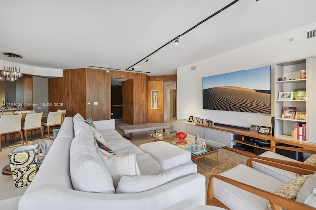 living area featuring wooden walls, visible vents, a chandelier, and track lighting