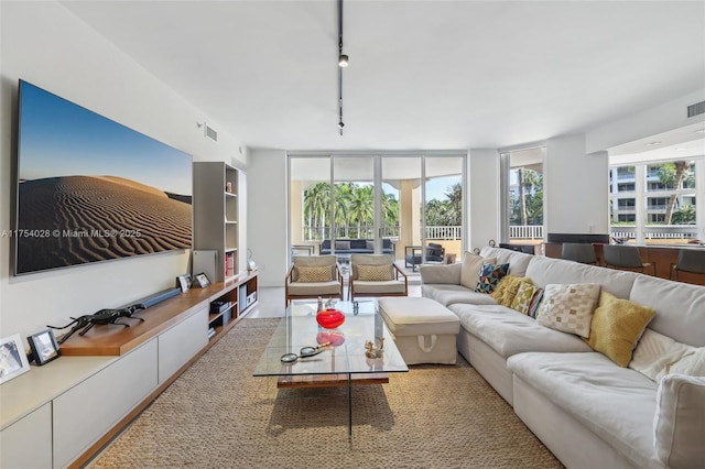 living room featuring rail lighting, plenty of natural light, visible vents, and a wall of windows