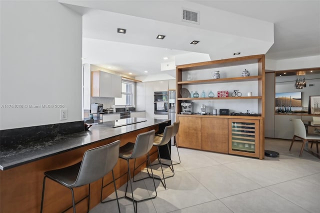 kitchen featuring light tile patterned floors, visible vents, wine cooler, a breakfast bar area, and black electric stovetop