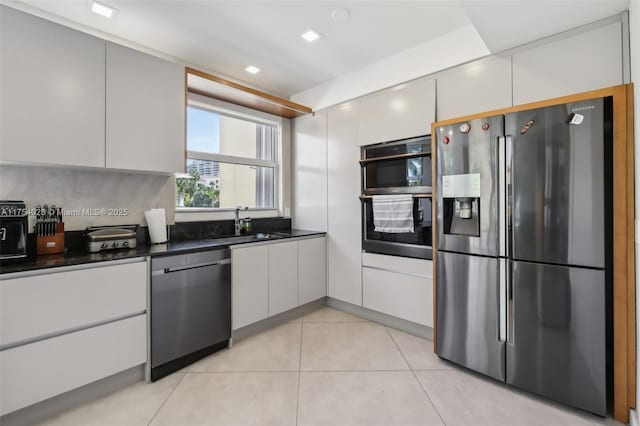 kitchen with light tile patterned floors, dark countertops, stainless steel appliances, white cabinetry, and a sink