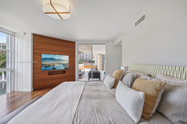 bedroom with expansive windows, visible vents, wooden walls, and wood finished floors