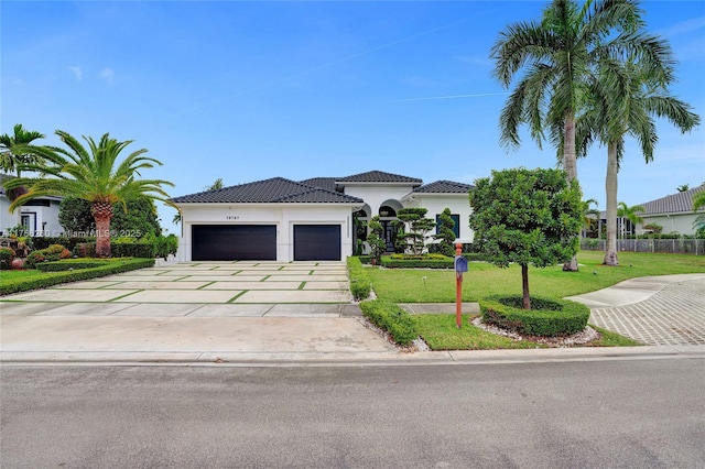 mediterranean / spanish-style home with a garage, concrete driveway, a tile roof, a front lawn, and stucco siding