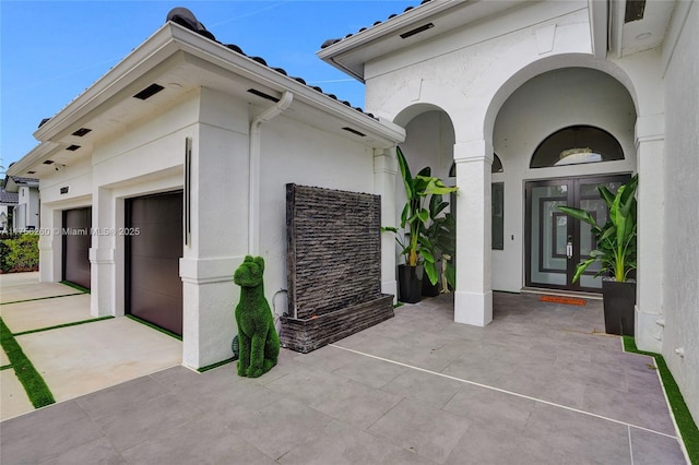 exterior space with an attached garage, elevator, concrete driveway, and french doors