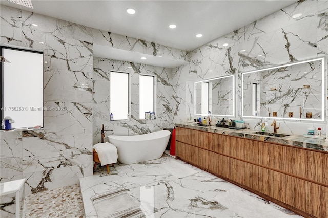 full bath featuring stone wall, marble finish floor, a freestanding tub, and a sink