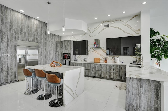 kitchen with light stone countertops, a sink, built in refrigerator, and modern cabinets