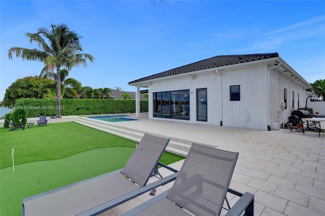 rear view of property featuring a tiled roof, a patio area, a fenced in pool, and stucco siding