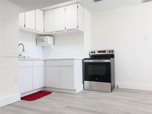 kitchen featuring white microwave, white cabinetry, light countertops, stainless steel electric range, and light wood finished floors