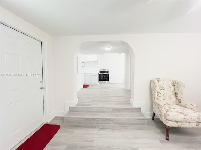 hallway featuring arched walkways, baseboards, and light wood finished floors