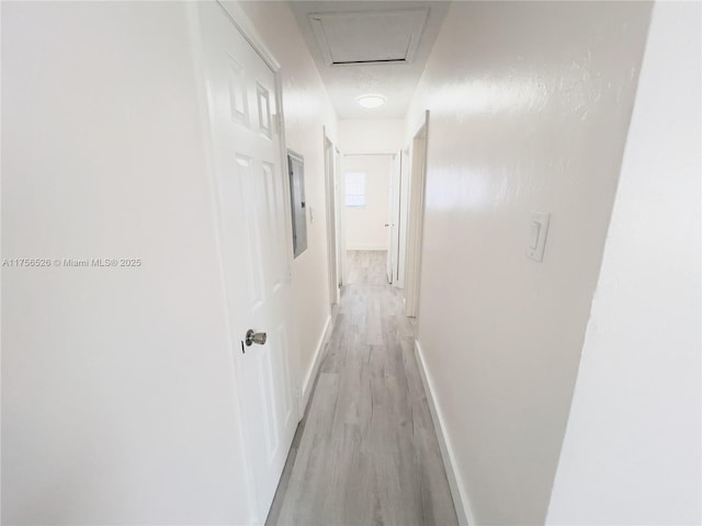 corridor with light wood-style floors, attic access, electric panel, and baseboards