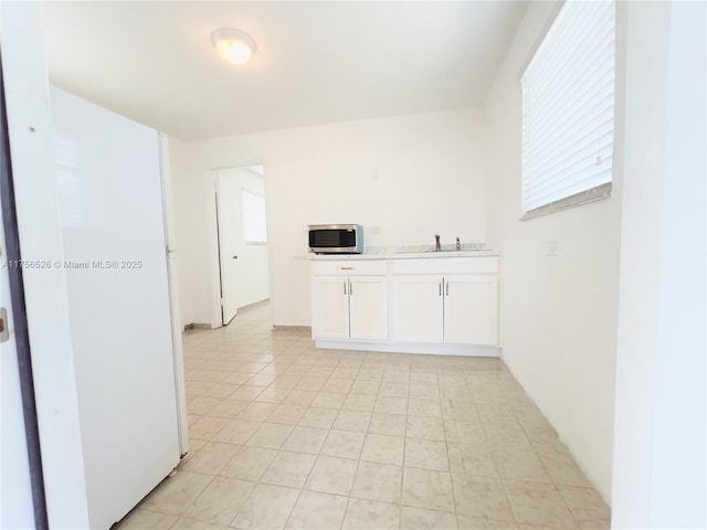 kitchen with light countertops, stainless steel microwave, a sink, and white cabinets