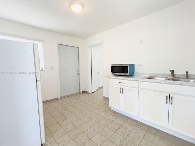 kitchen with baseboards, white cabinets, stainless steel microwave, freestanding refrigerator, and a sink