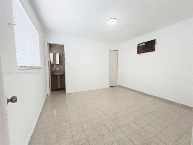 spare room featuring an AC wall unit, a sink, and baseboards