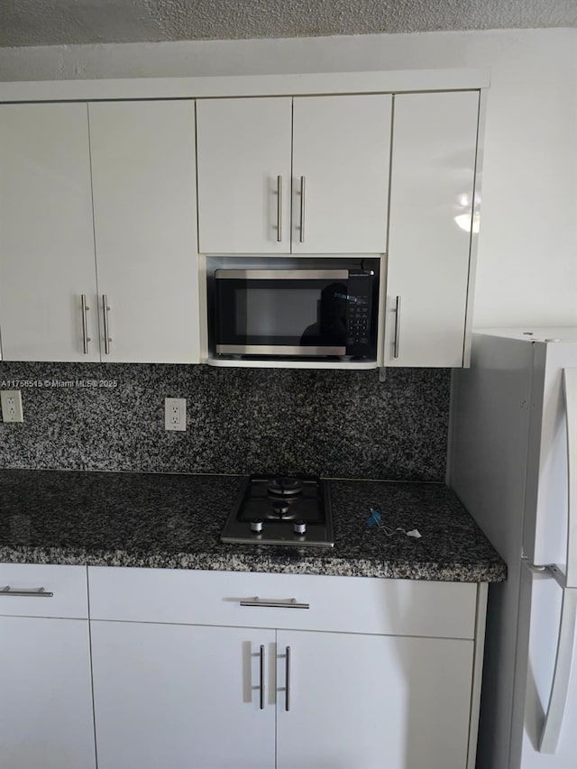 kitchen featuring dark stone counters, appliances with stainless steel finishes, backsplash, and white cabinetry