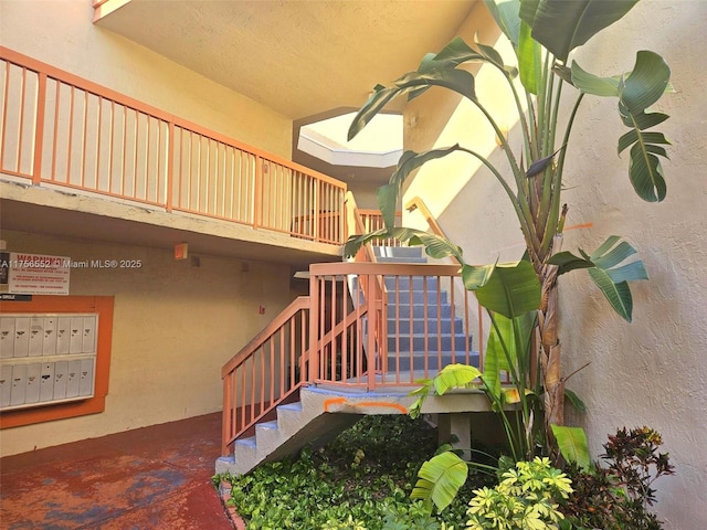 stairway with unfinished concrete floors, mail area, and a textured wall