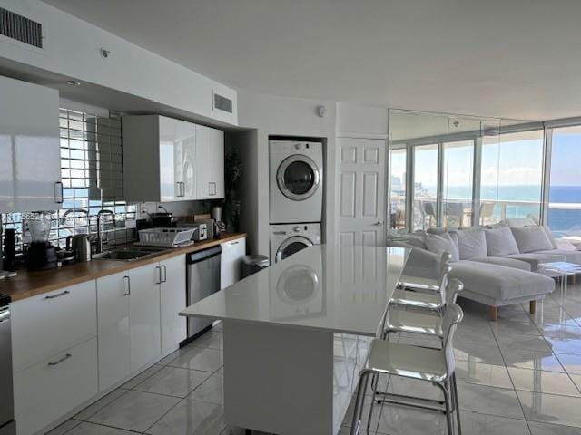 kitchen featuring stacked washer and dryer, visible vents, white cabinets, a sink, and dishwasher