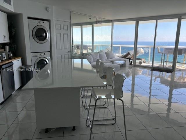 kitchen with light tile patterned flooring, a water view, white cabinetry, stacked washing maching and dryer, and dishwasher