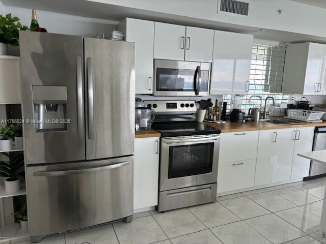 kitchen featuring visible vents, appliances with stainless steel finishes, white cabinets, a sink, and butcher block countertops