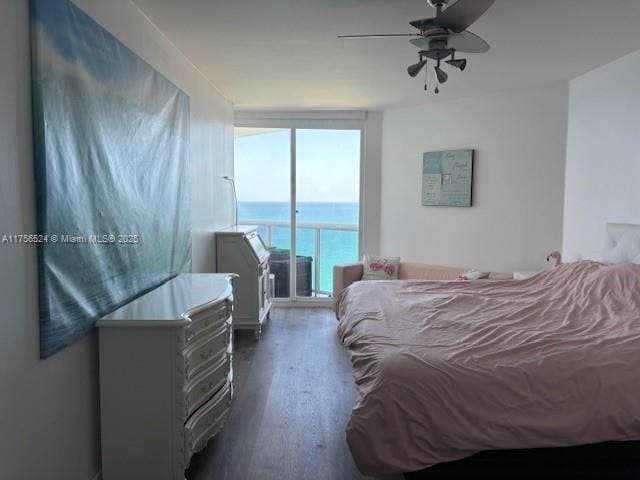 bedroom featuring a ceiling fan, dark wood-style floors, a water view, access to exterior, and a wall of windows