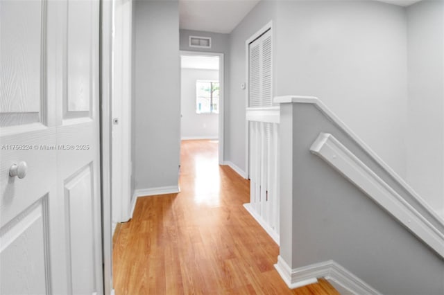 hallway with visible vents, light wood finished floors, an upstairs landing, and baseboards