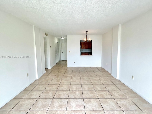 empty room featuring light tile patterned floors, visible vents, a chandelier, and a textured ceiling