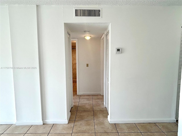 hallway with light tile patterned floors, a textured ceiling, visible vents, and baseboards