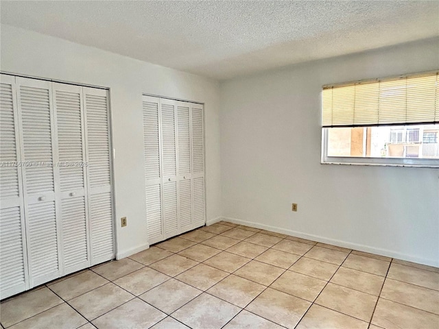 unfurnished bedroom featuring a textured ceiling, light tile patterned floors, baseboards, and multiple closets