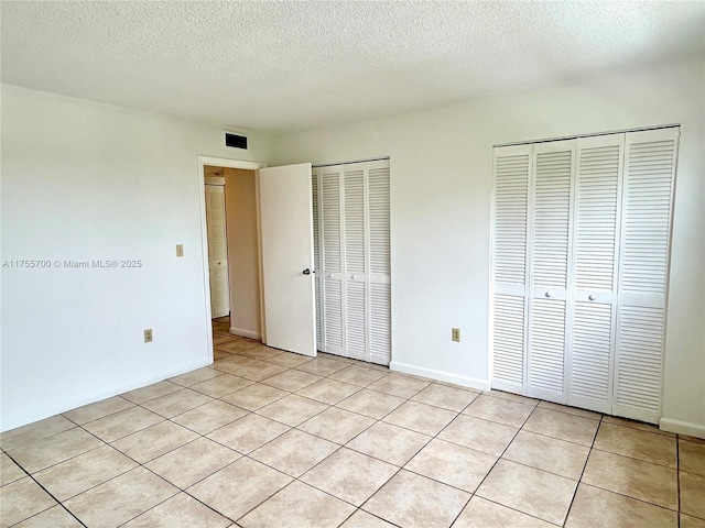 unfurnished bedroom featuring multiple closets, visible vents, a textured ceiling, and baseboards