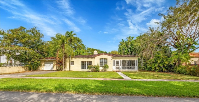 mediterranean / spanish-style home with aphalt driveway, a sunroom, a chimney, and a front lawn