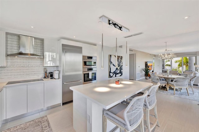 kitchen with an inviting chandelier, wall chimney exhaust hood, modern cabinets, stainless steel appliances, and backsplash