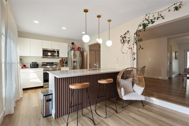 kitchen with light wood finished floors, appliances with stainless steel finishes, light countertops, a kitchen bar, and white cabinetry