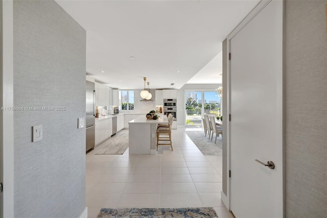 kitchen featuring a kitchen island, a breakfast bar area, appliances with stainless steel finishes, light tile patterned flooring, and white cabinetry