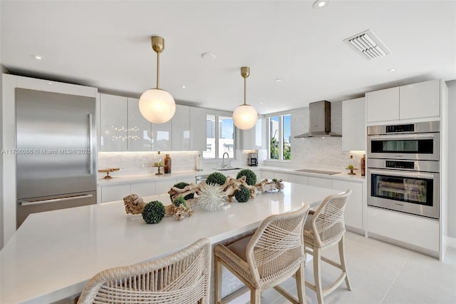 kitchen featuring tasteful backsplash, visible vents, wall chimney exhaust hood, a kitchen bar, and appliances with stainless steel finishes