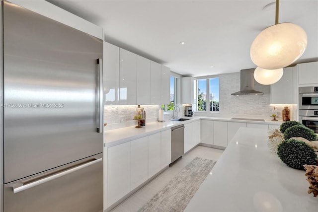 kitchen with modern cabinets, a sink, appliances with stainless steel finishes, wall chimney exhaust hood, and decorative backsplash