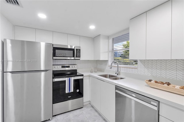 kitchen featuring visible vents, white cabinets, stainless steel appliances, light countertops, and a sink