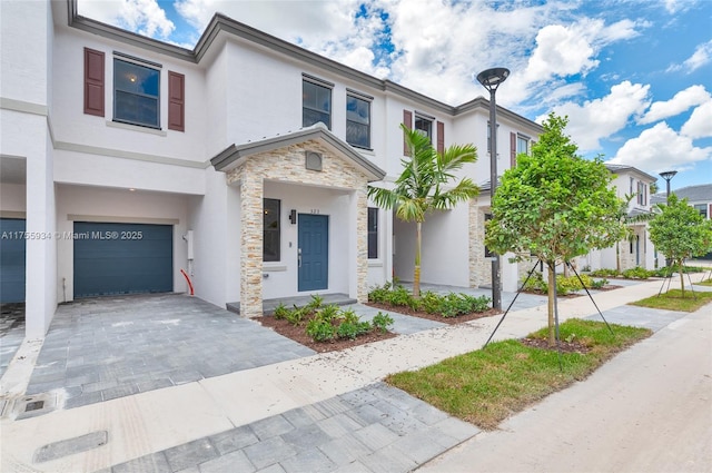 townhome / multi-family property with stone siding, decorative driveway, an attached garage, and stucco siding